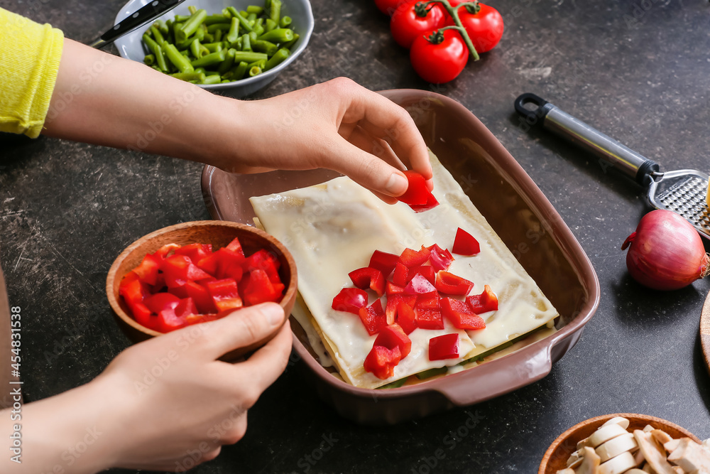 Woman preparing tasty vegetable lasagna on dark background