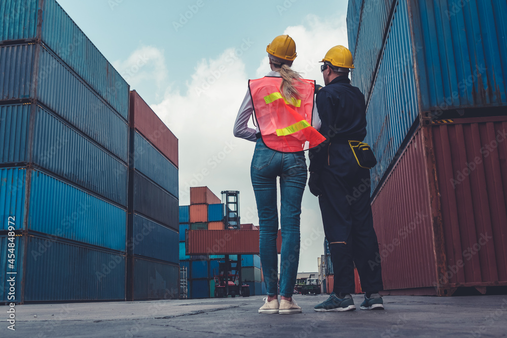 Industrial worker works with co-worker at overseas shipping container yard . Logistics supply chain 