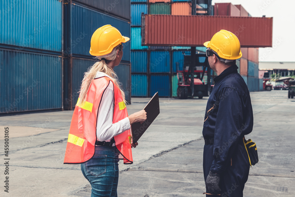 Industrial worker works with co-worker at overseas shipping container yard . Logistics supply chain 