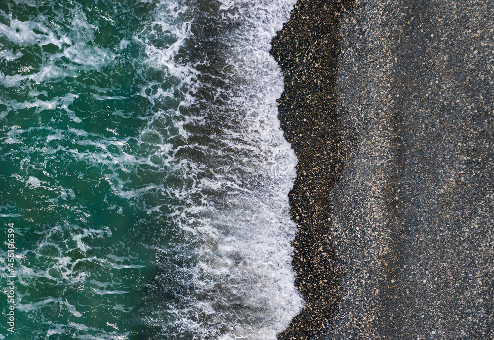 绿色海浪拍打着黑色的沙滩和卵石海岸，空中海洋纹理