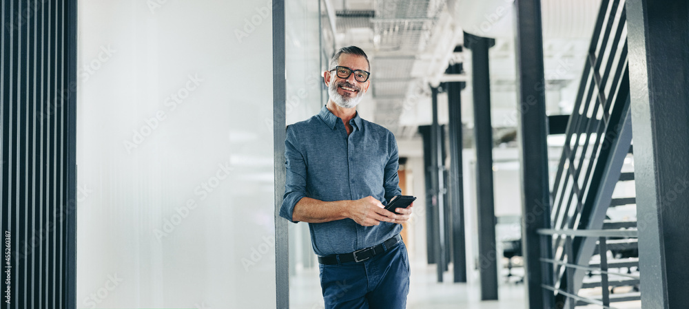 Smiling mature businessman holding a smartphone in an office