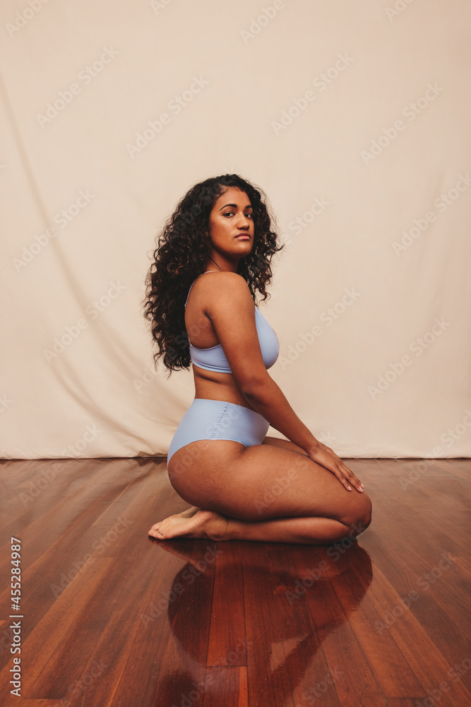 Young woman kneeling while wearing blue underwear in a studio