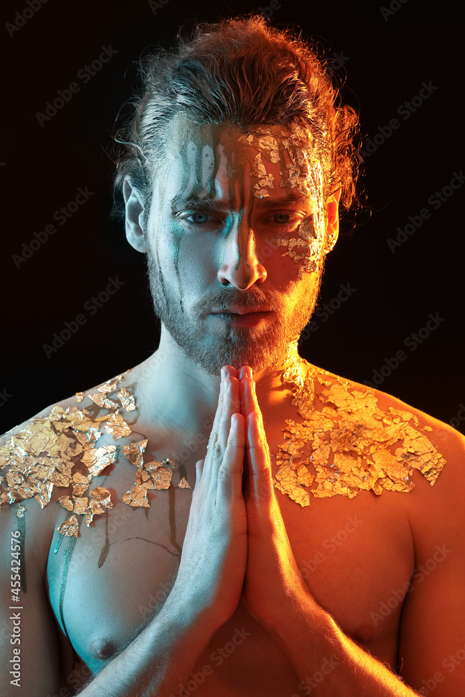 Handsome young man with golden paint on body against black background