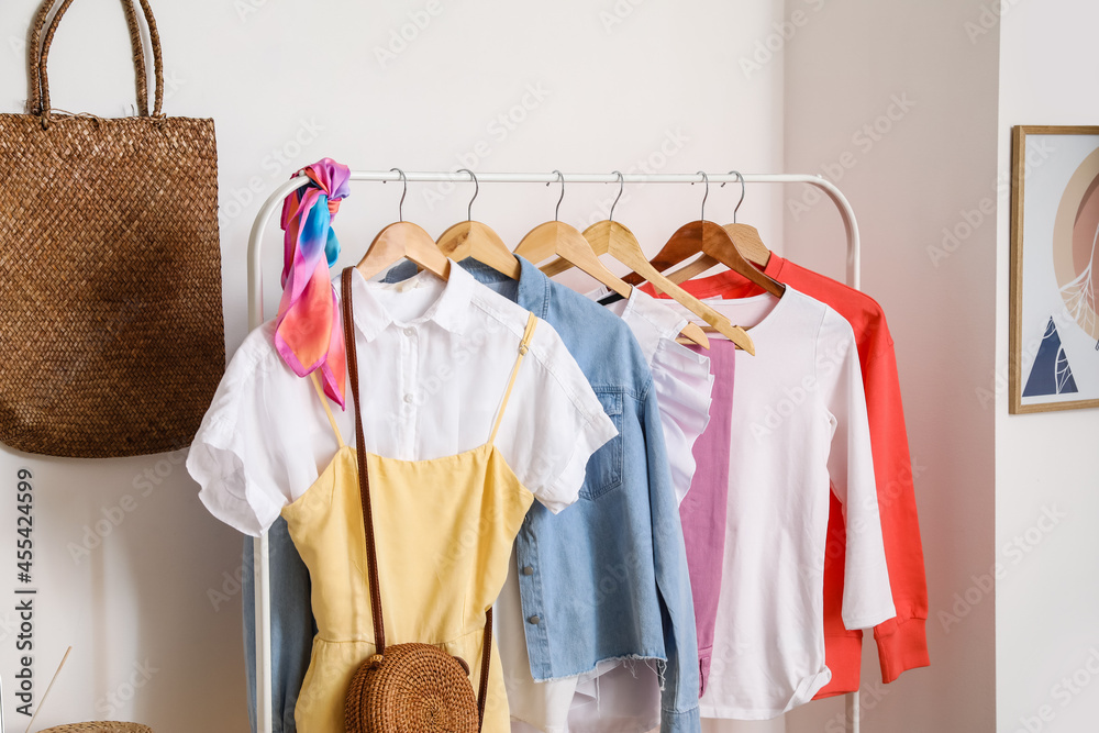 Rack with stylish clothes near light wall