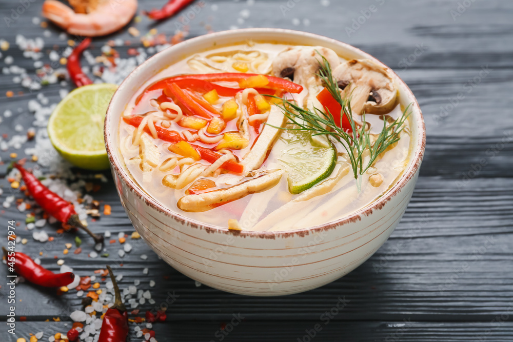 Bowl of tasty Thai soup with chicken on dark wooden background