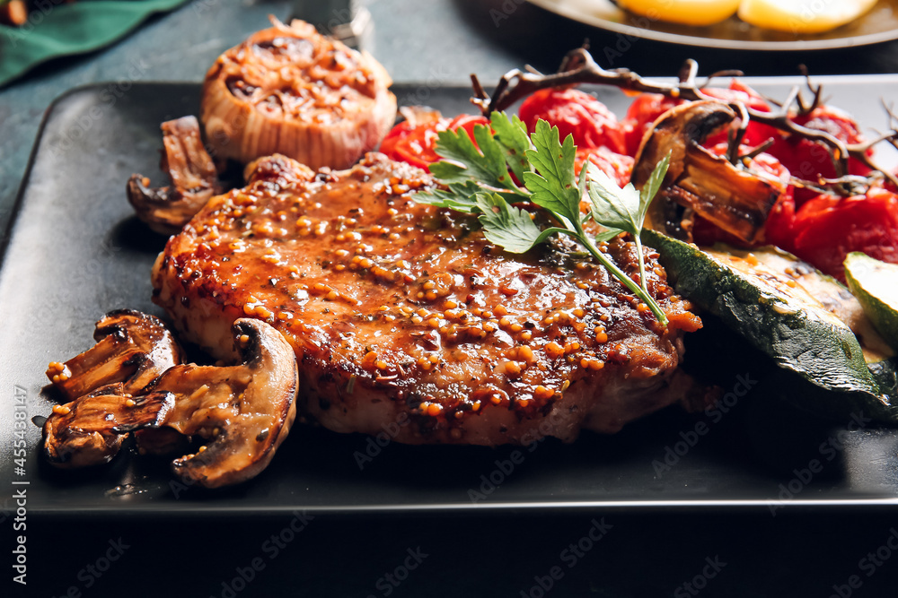 Plate with tasty pork steak and vegetables on dark background, closeup