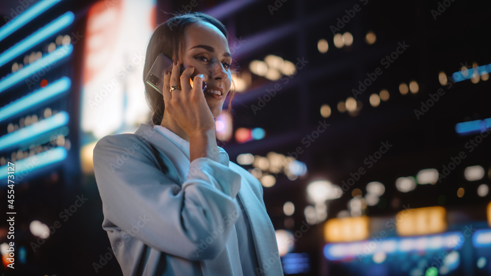 美丽的年轻女子在充满霓虹灯的夜城街道上用智能手机聊天。Po