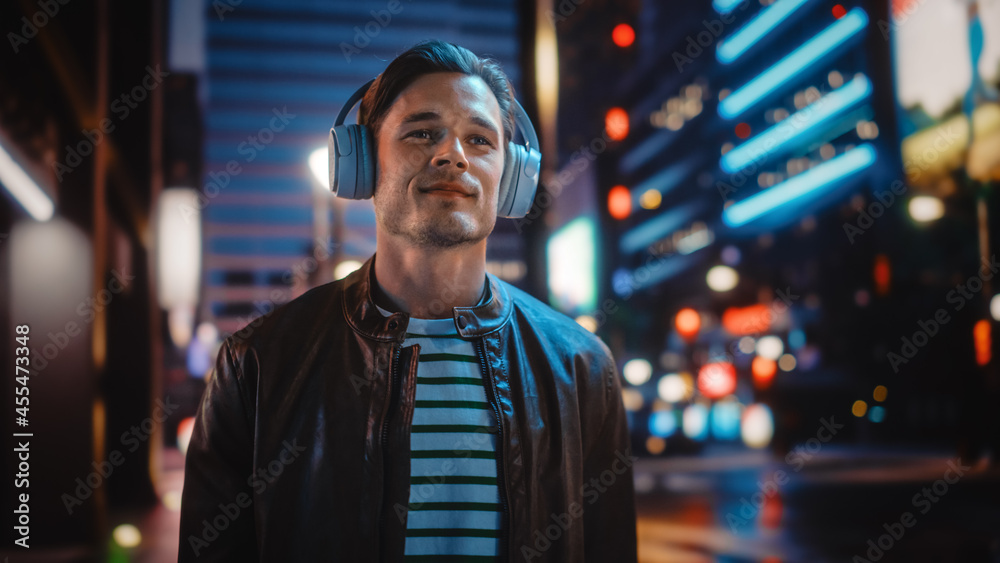 Portrait of Handsome Man Wearing Headphones Walking Through Night City Street Full of Neon Light. Sm