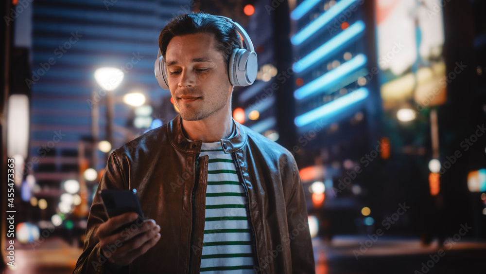 Portrait of Handsome Man Wearing Headphones Walking Through Night City Street Full of Neon Light. Sm