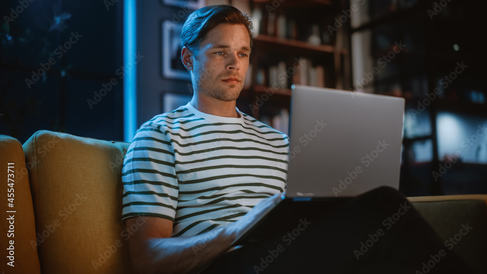 Man Using Laptop at Home Office, Does Remote Work in the Evening. Handsome Male Sitting on Sofa Work