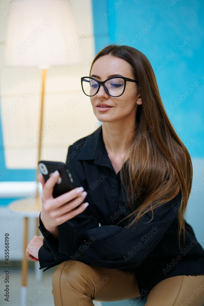 令人惊叹的美丽女孩微笑着，戴着现代眼镜对着镜头摆姿势。女人坐着看