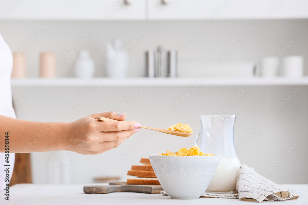 Woman eating tasty corn flakes in kitchen