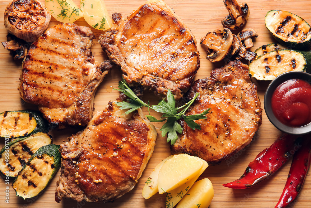 Tasty pork steaks, tomato sauce and grilled vegetables on wooden background