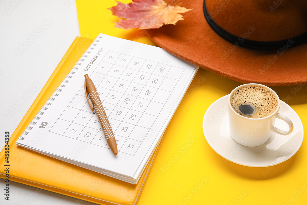 Calendar with cup of coffee, hat and notebook on color background, closeup