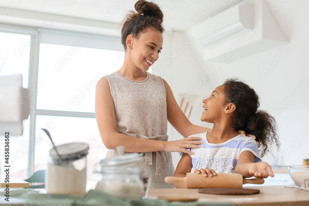 African-American little girl and her mother rolling out dough in kitchen