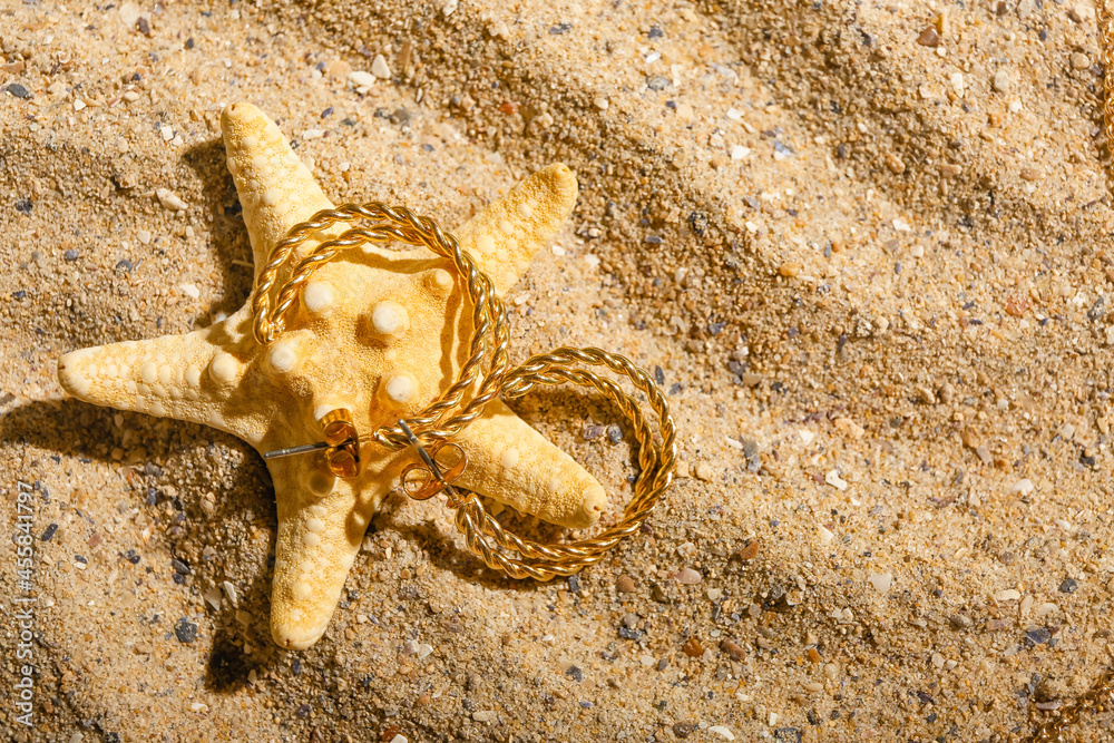 Stylish earrings and starfish on sand