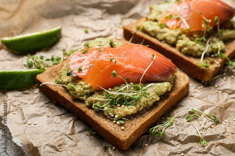 Tasty sandwiches with guacamole and salmon in parchment on table, closeup