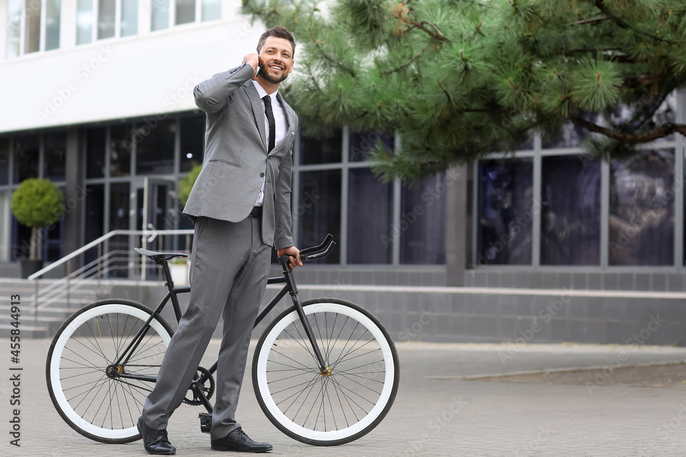 Businessman with bicycle and mobile phone on city street