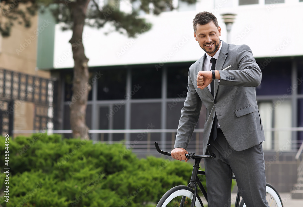 Businessman with bicycle looking at wrist watch on city street