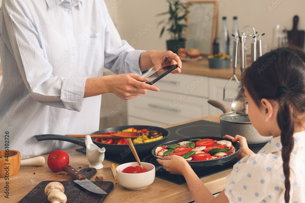 女儿和妈妈拿着手机在厨房拍美食