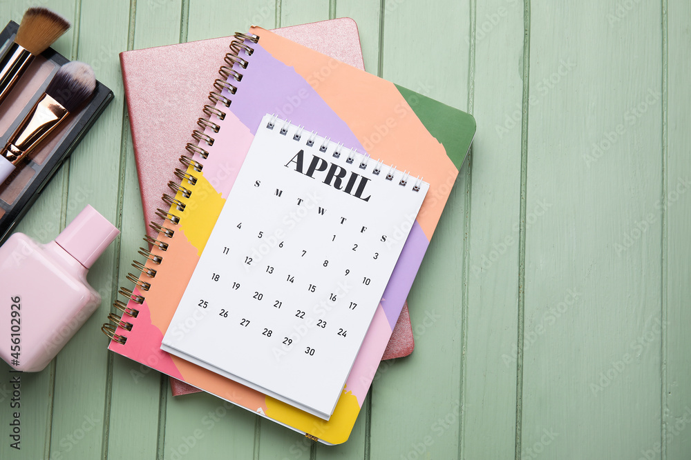 Calendar with decorative cosmetics and notebooks on color wooden background