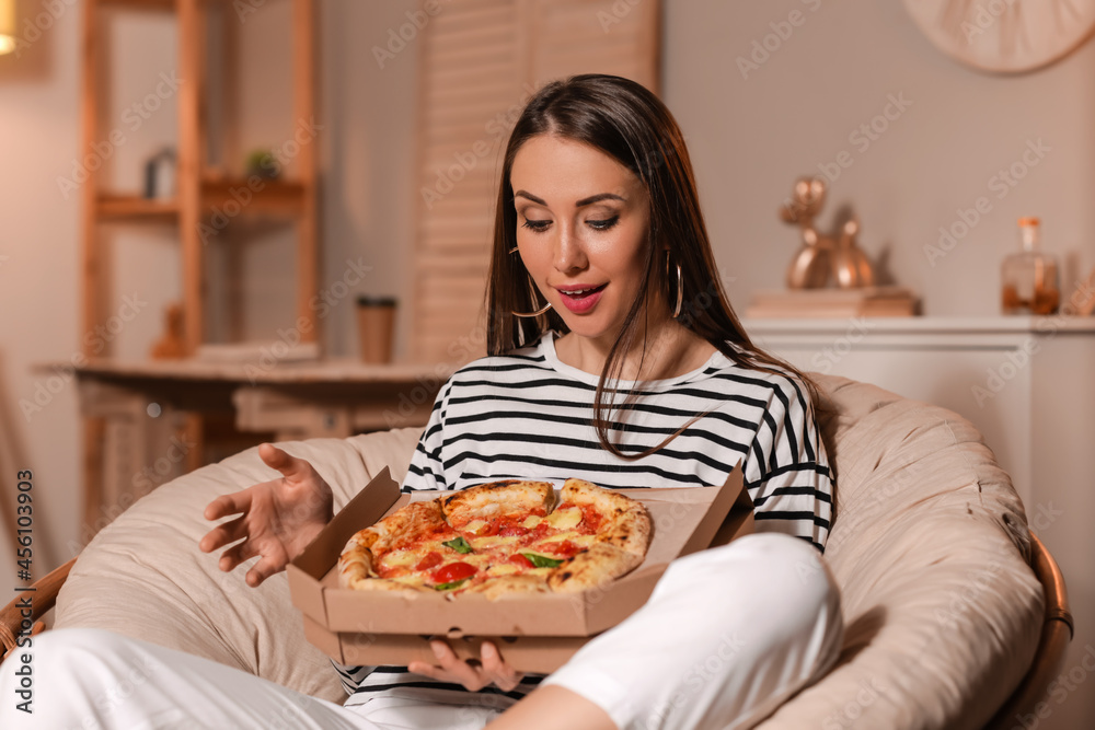 Beautiful young woman eating tasty pizza at home in evening