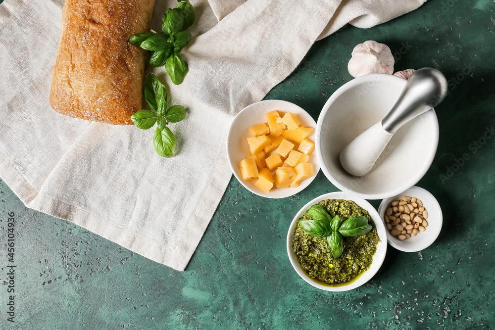 Bowl with tasty pesto sauce, cheese and pine nuts on color background