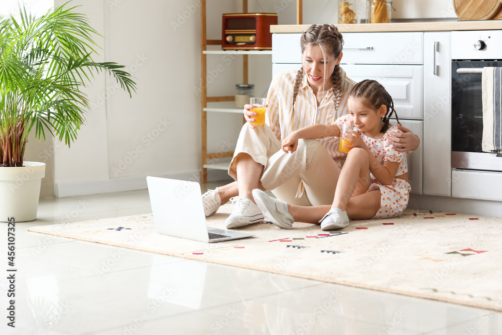 Little girl and her mother drinking juice while watching cartoons in kitchen