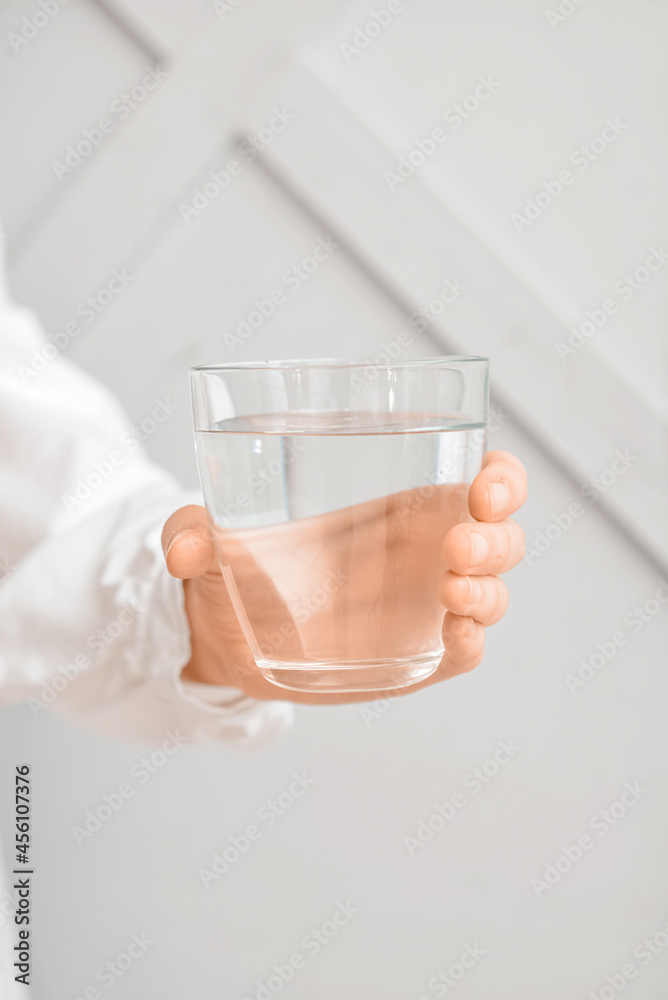 Female hand with glass of water on light background, closeup