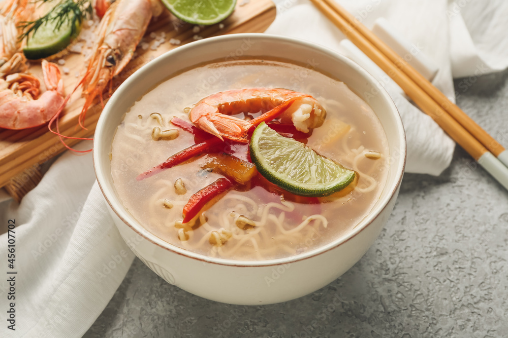 Bowl of tasty Thai soup with shrimps on grey background