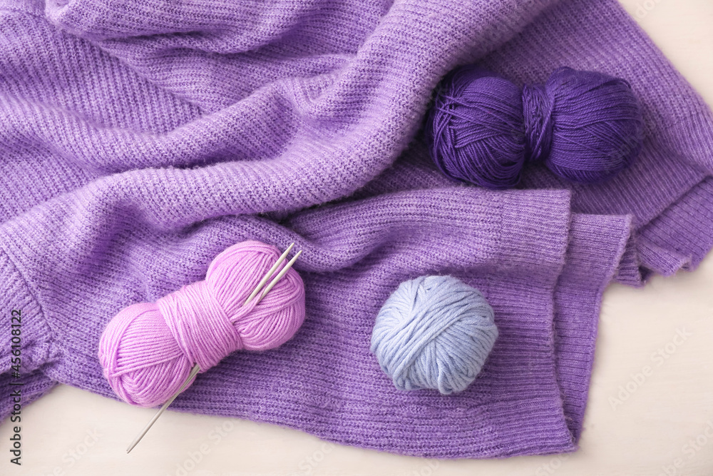 Yarn with knitting needles and sweater on white background