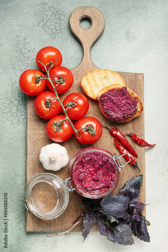 Wooden board with jar of tasty pesto sauce and ingredients on light background