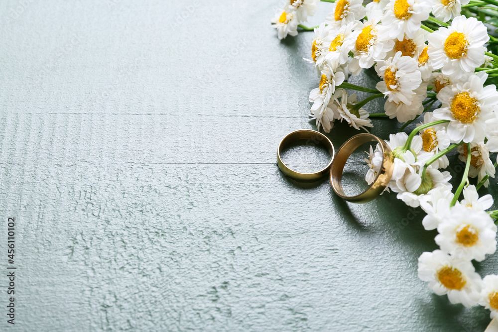 Wedding rings and chamomile flowers on color wooden table