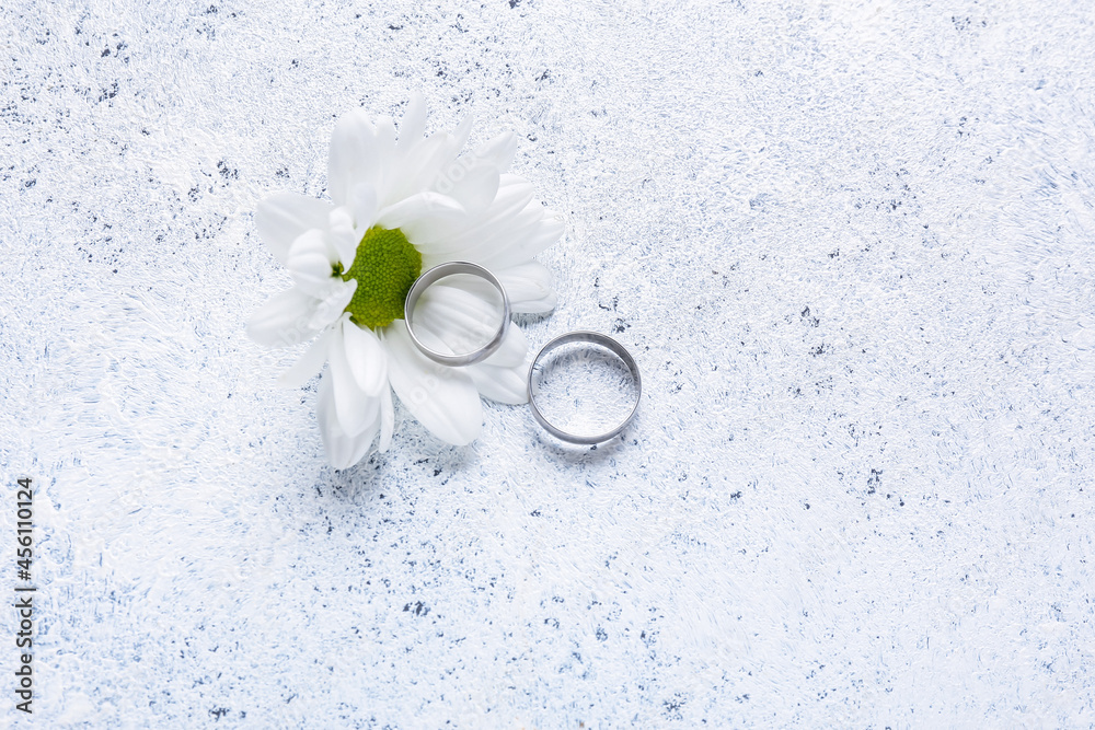 Wedding ring and chamomile flower on light background