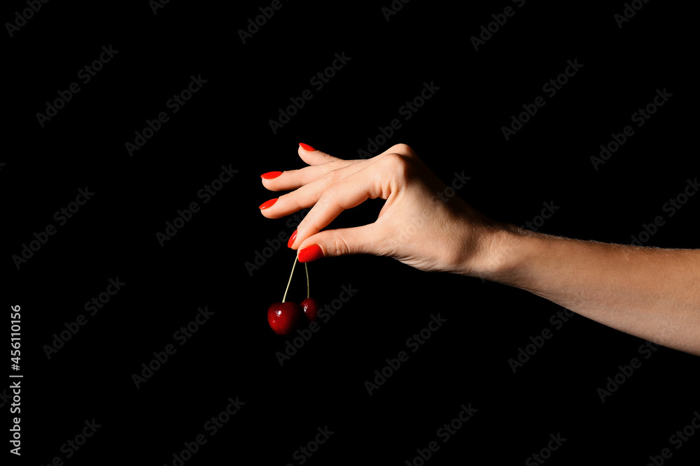 Woman with beautiful manicure holding cherry on dark background