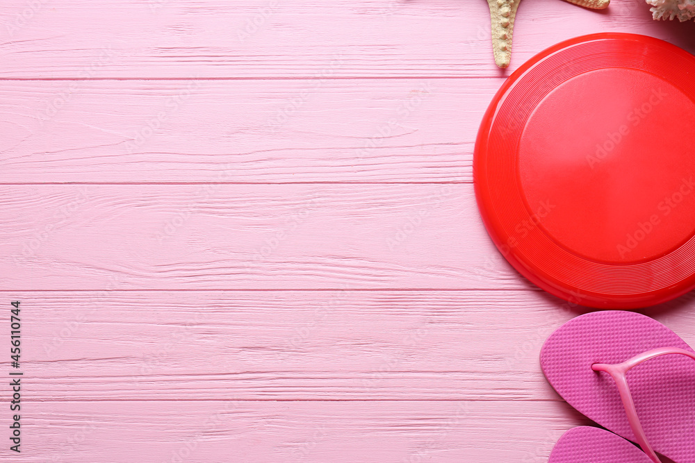 Frisbee disk and flip-flops on color wooden background