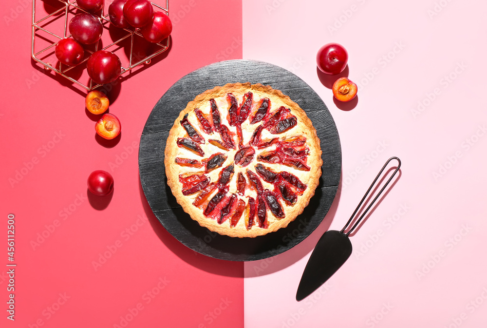 Board with tasty plum pie on color background