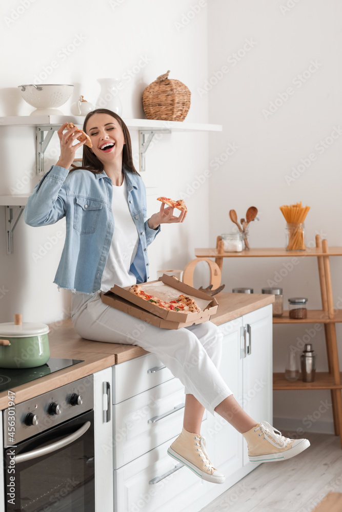 美丽的年轻女子在厨房吃美味的披萨