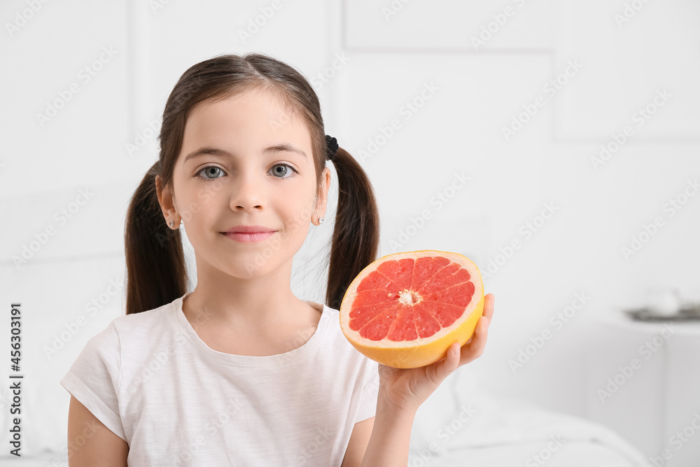 Little girl with fresh tasty grapefruit in bedroom