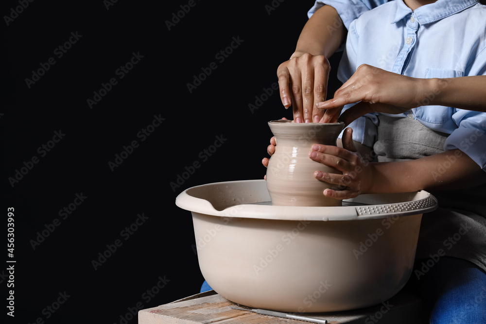 Little girl with her mother making ceramic pot on dark background