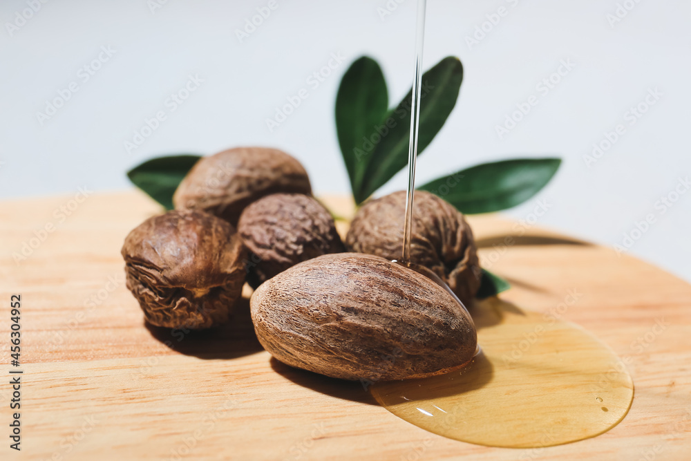 Pouring of essential oil onto board with shea nuts on light background, closeup