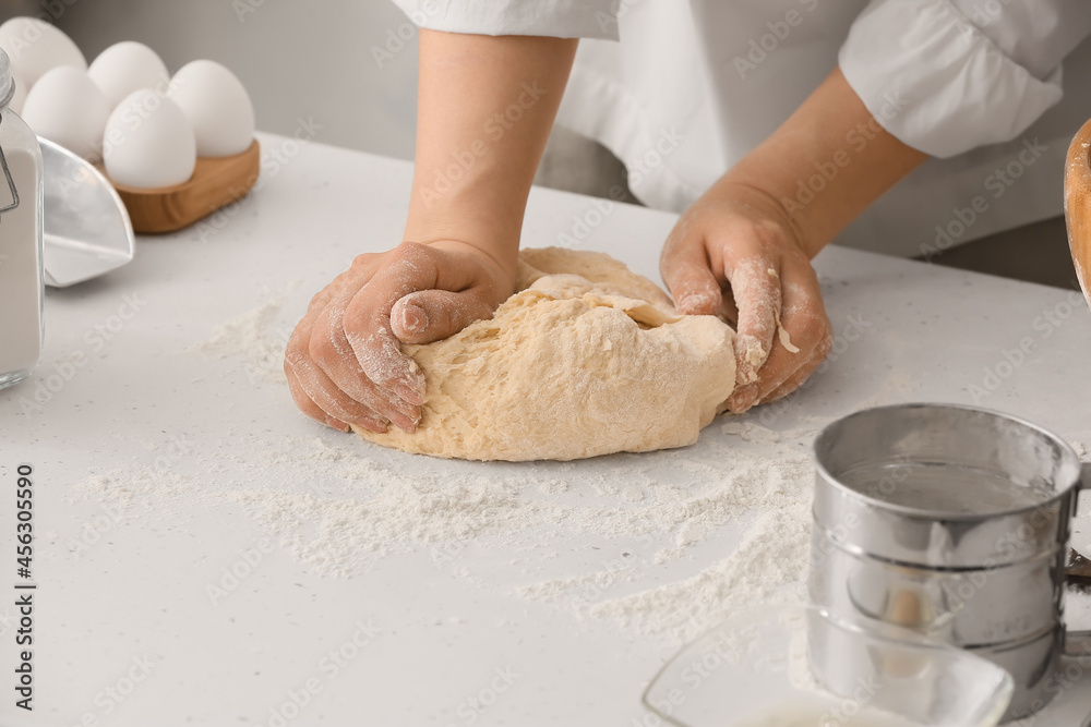 Female chef preparing dough on kitchen table, closeup