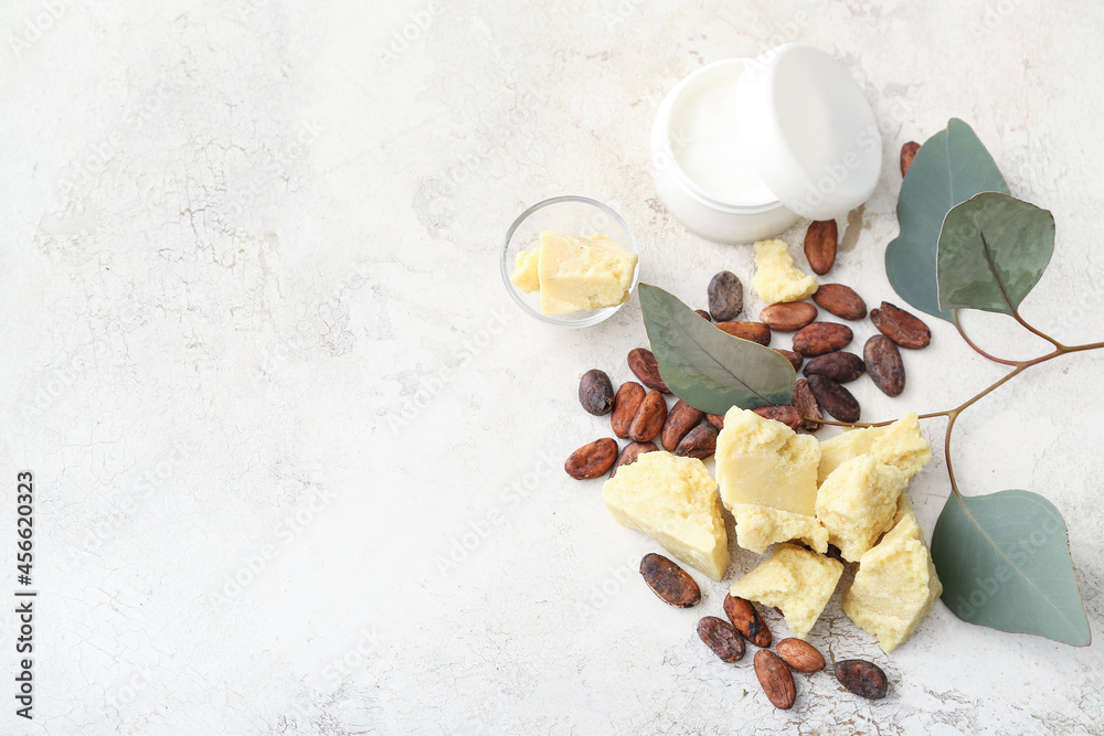 Pieces of cocoa butter, beans and jar of cream on light background