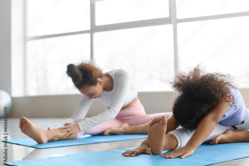 African-American little girl with her mother practicing yoga at home