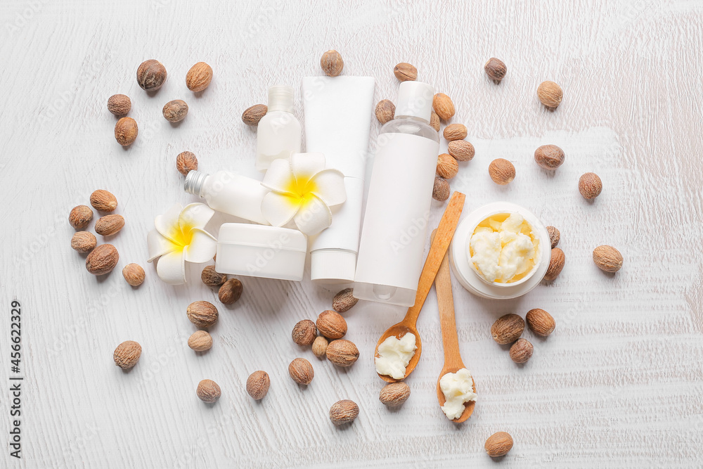 Jar of shea butter, nuts and cosmetic products on light background