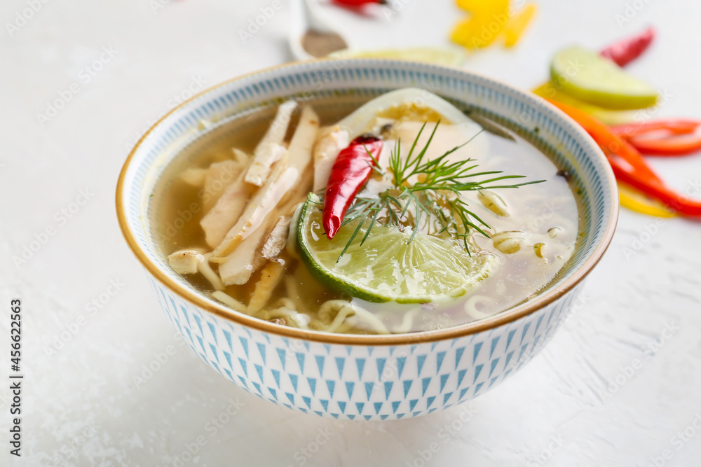 Bowl of tasty Thai soup with chicken on light background