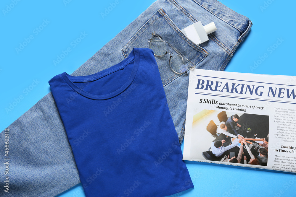 Stylish t-shirt, jeans, bottle of perfume, eyeglasses and newspaper on color background