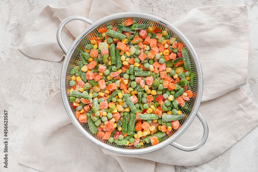 Colander with mix of frozen vegetables on light background, closeup