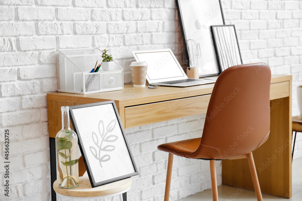 Stylish workplace with modern painting in frame near white brick wall