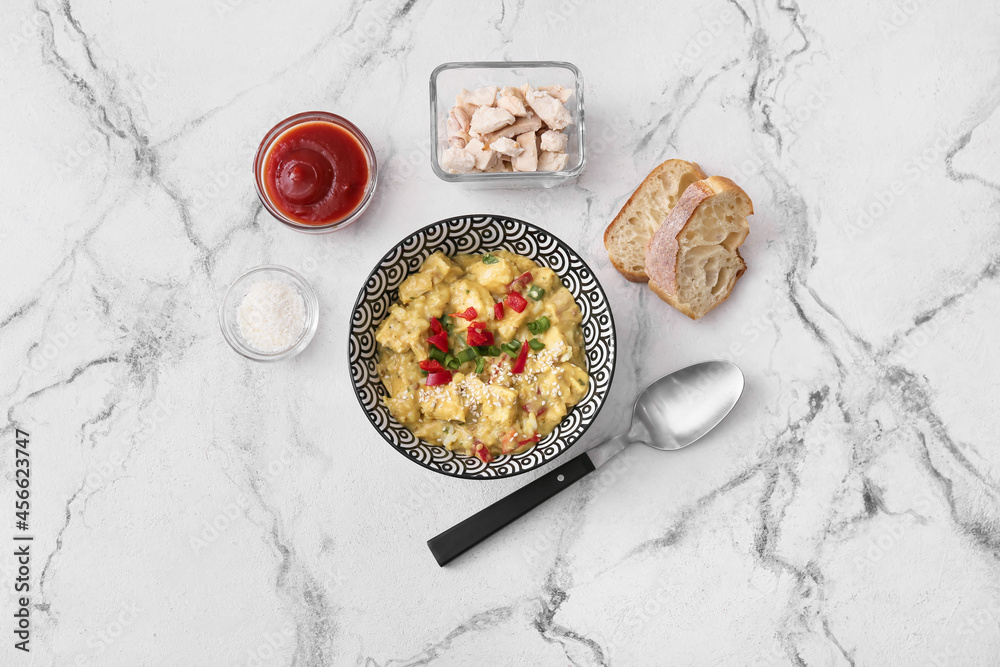 Bowl of tasty chicken curry and ingredients on light background